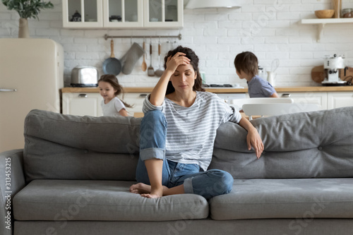 Fényképezés Exhausted mother sitting on couch while kids running at home