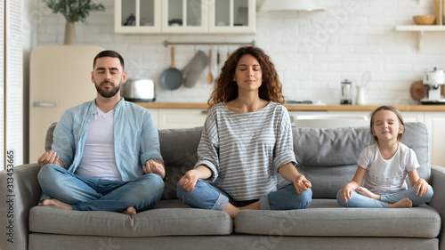 Couple and little daughter sitting on couch do meditation indoors