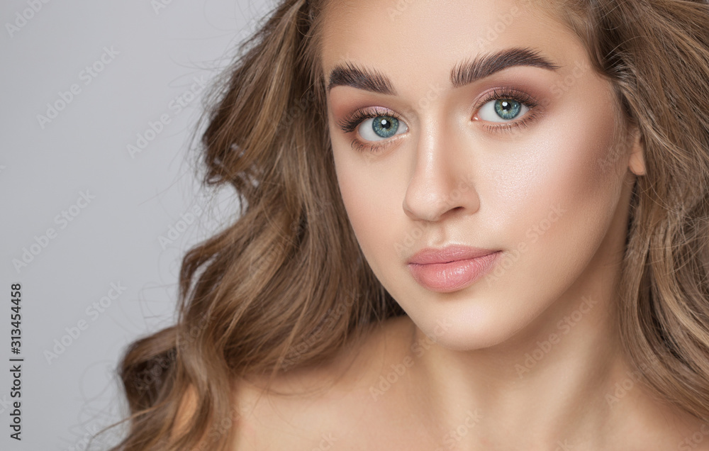 Obraz premium Portrait of a beautiful woman with long eyelashes, beautiful fresh nude make-up, thick eyebrows and with clean skin in a beauty salon. Eyelash extensions. Face close-up.Make-up and cosmetology concept