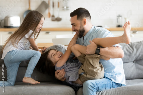 Active cheerful father playing with children on couch at home