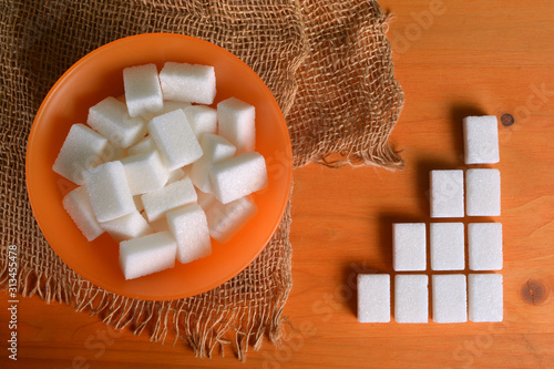 Orange sugar bowl full of sugar cubes on wooden table with alongside graphical composition. photo
