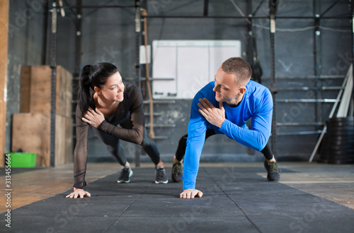 Man and woman doing pushups at training in gym.