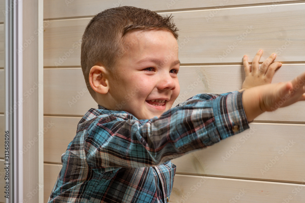 A 4 years old boy in a blue clerical shirt is crying on a light wooden background. A 4 years old boy in a blue clerical shirt is crying on a light wooden background.