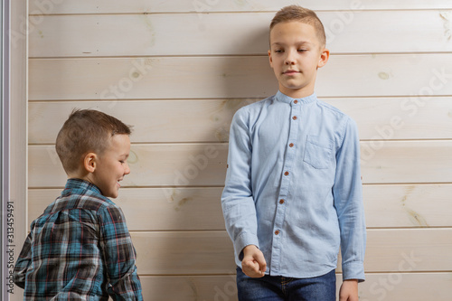 A 4-year-old boy in a blue klepy shirt cries on a light wooden background and his brother, 10 years old, is standing. photo