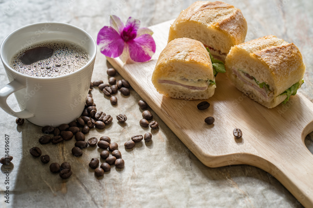 ham cheese baguette, cup coffee on textured tile table. ham cheese baguette, cup coffee on textured tile table.