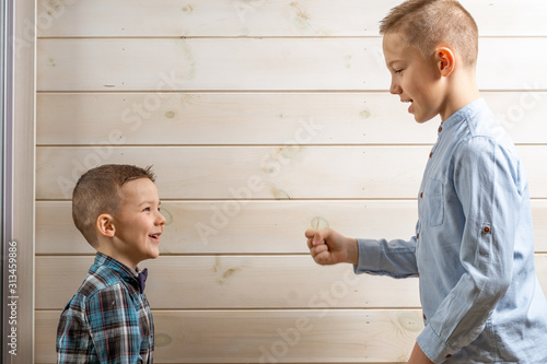 A 4-year-old boy in a blue klepy shirt cries on a light wooden background and his brother, 10 years old, is standing. photo