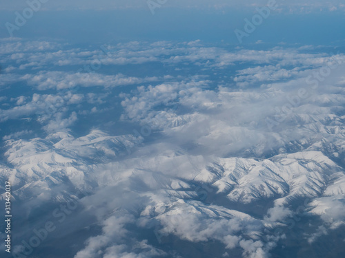 Aerial view of snow covered french and spanish pyrenees with snow covered mountains viewed from an aeroplane. Blue sky white clouds background