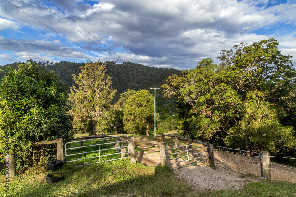 Rural property in Australia, gate leads to dirt tracks and woodlands large tree covered hill in the distance