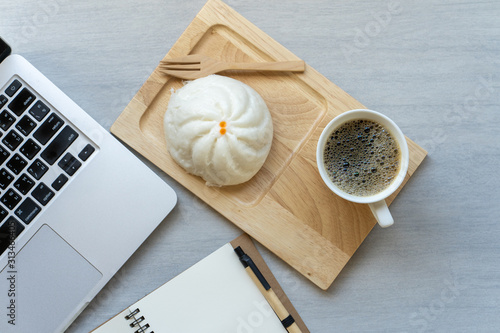 Cup coffee, steamed bun, notepad and laptop on texture white table.