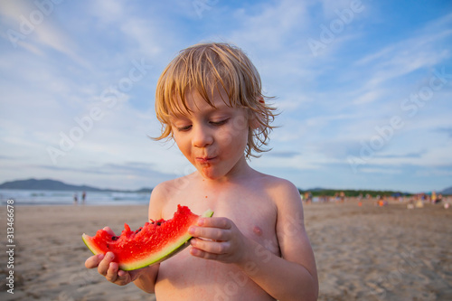 Little boy eats a watermelon on the beach.