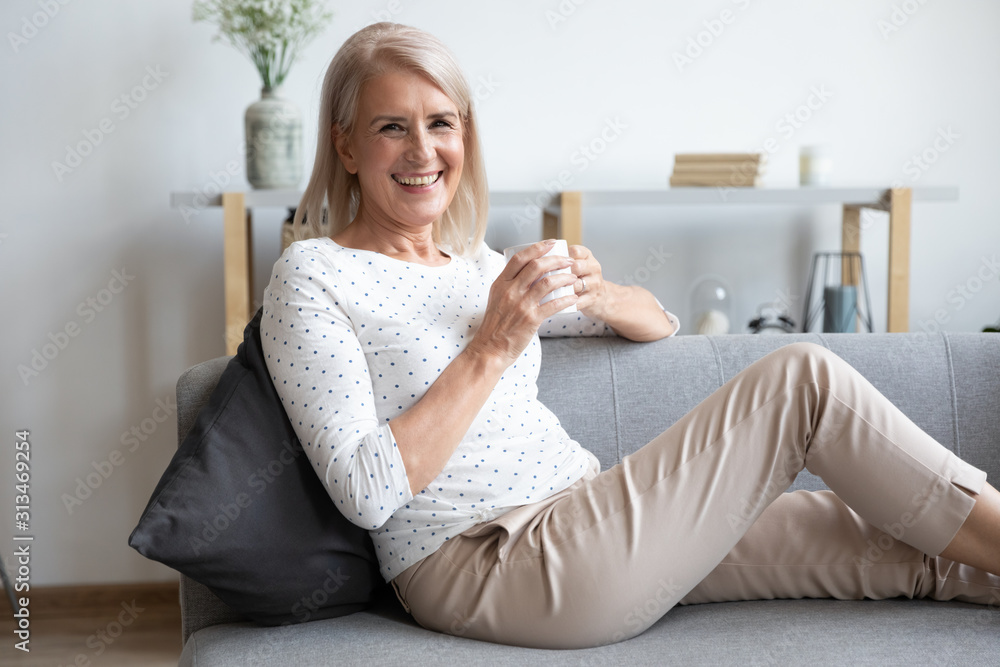 Portrait of smiling mature woman relaxing on couch with cup - obrazy, fototapety, plakaty 