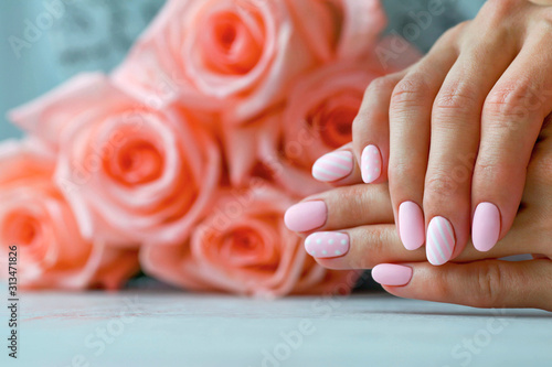 Slika na platnu Beautiful pink matte manicure against the background of  roses