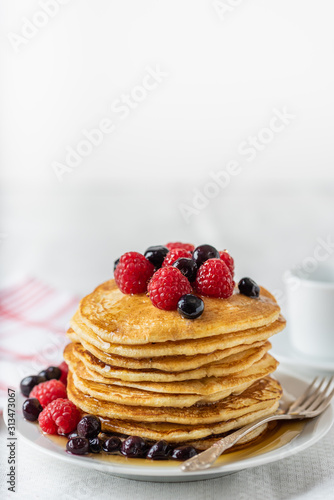 Sweet homemade pancakes with raspberries and blueberries on white plate.