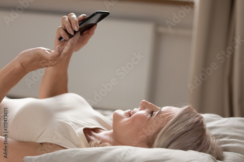 Happy senior woman relax in bed using cellphone at home