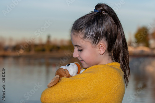 girl with a yellow sweater hugging a teddy near a lake