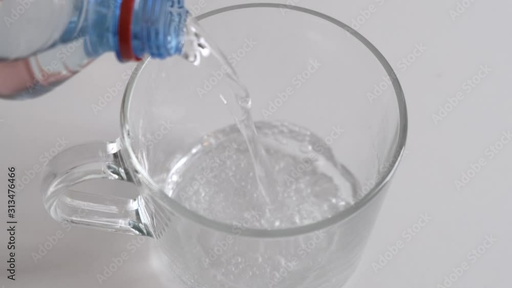Pour a transparent glass with cold water from bottle on white background. Close up. Pour a transparent glass with cold water from bottle on white background. Close up.