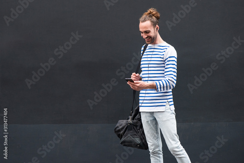 young man with mobile phone and earphones by black background © mimagephotos
