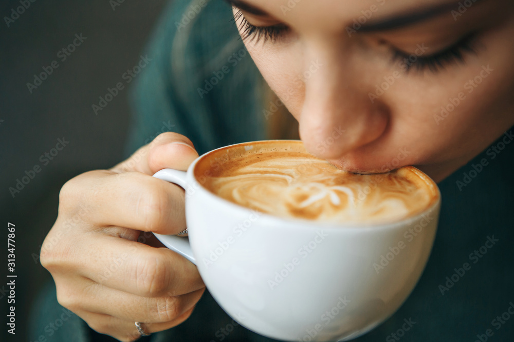 Close up girl is drinking coffee. She enjoys her morning cappuccino or flat white.