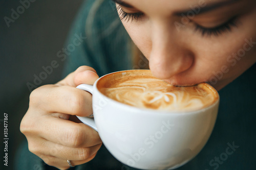 Close up girl is drinking coffee. She enjoys her morning cappuccino or flat white. photo