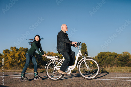 Fototapeta Naklejka Na Ścianę i Meble -  Young girl on roller skates and a man on a electric bike fun ride together. Active leisure and hobbies. Father and daughter.