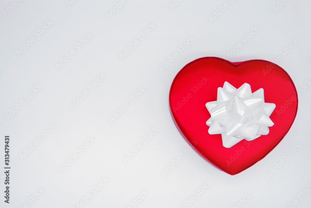Bright red satin heart-shaped box with a large white flower bow on a white background. Concept of love, Valentine's day, gift, beloved, surprise, present, feelings of love. Isolated