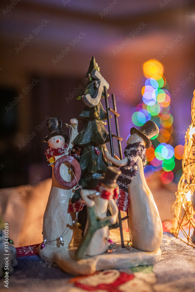 Naklejka premium Snowmen decorating a Chistmas Tree with boken from a real tree behind them