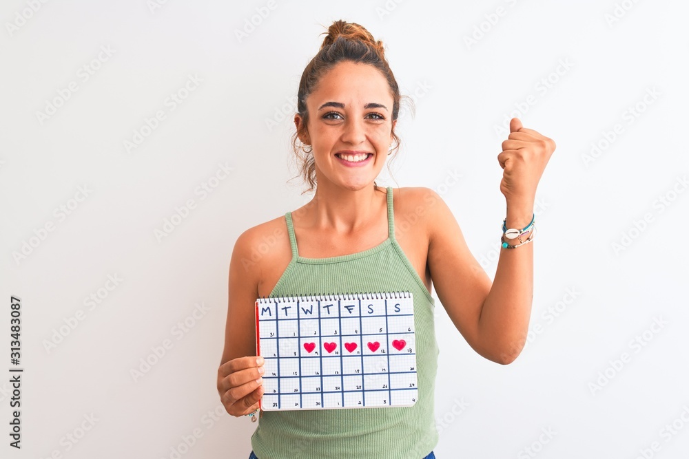 Young redhead woman holding menstruation calendar over isolated background screaming proud and celebrating victory and success very excited, cheering emotion Young redhead woman holding menstruation calendar over isolated background screaming proud and celebrating victory and success very excited, cheering emotion