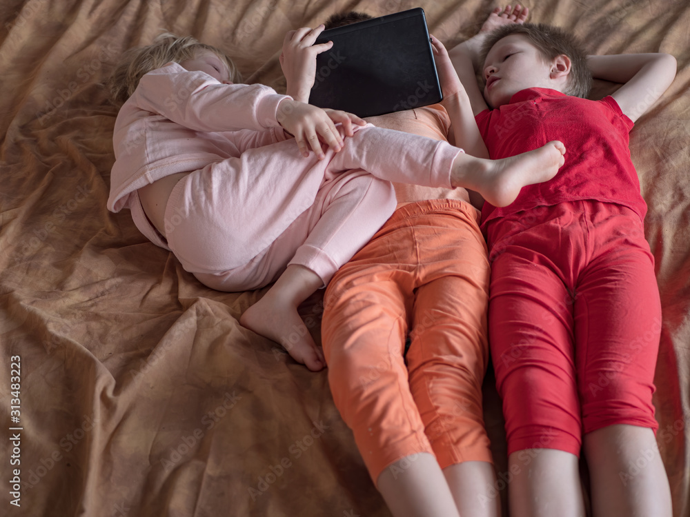 Three boys brothers are sitting on couch and playing computer game on tablet. Children are happy together at home. kids in home pajamas Three boys brothers are sitting on couch and playing computer game on tablet. Children are happy together at home. kids in home pajamas