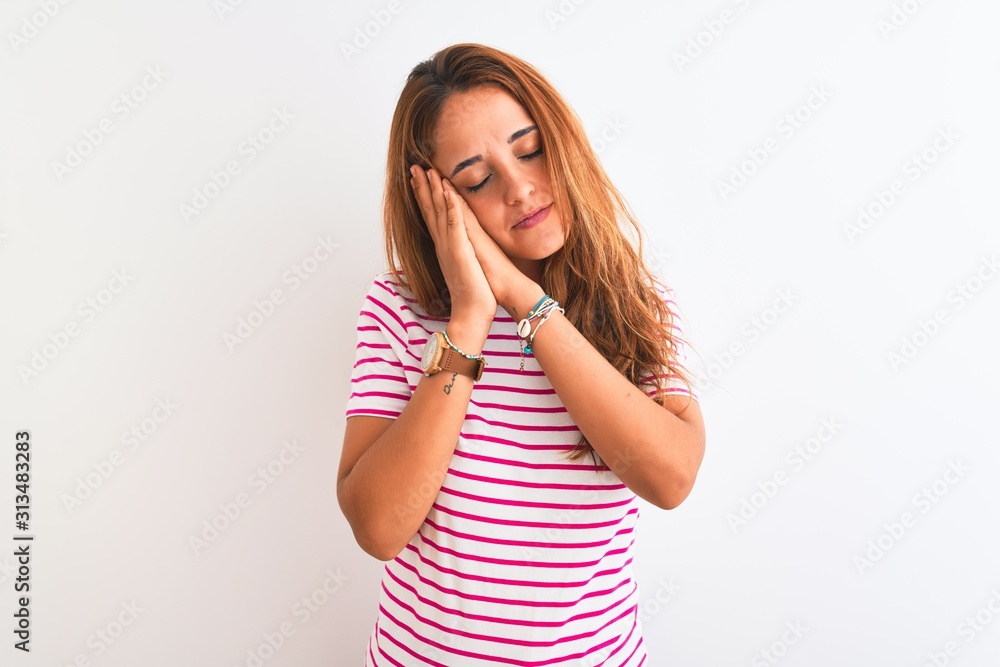 Young redhead woman wearing striped casual t-shirt stading over white isolated background sleeping tired dreaming and posing with hands together while smiling with closed eyes. Young redhead woman wearing striped casual t-shirt stading over white isolated background sleeping tired dreaming and posing with hands together while smiling with closed eyes.