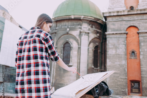 Woman is painting directly on the city street against the background of old architecture. Young girl artist is resting painting a picture © Andrii 