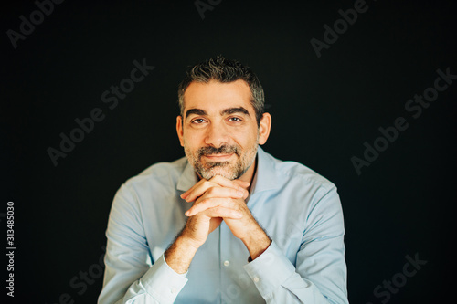 Portrait of handsome man wearing blue shirt, leaning on hands, posing on black background