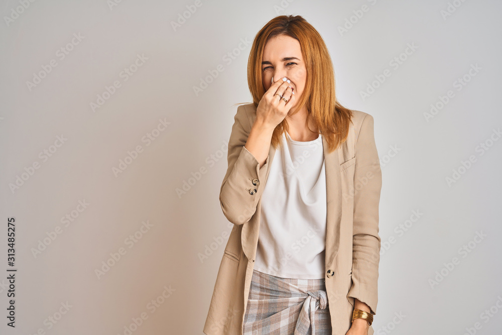 Redhead caucasian business woman standing over isolated background smelling something stinky and disgusting, intolerable smell, holding breath with fingers on nose. Bad smells concept. Redhead caucasian business woman standing over isolated background smelling something stinky and disgusting, intolerable smell, holding breath with fingers on nose. Bad smells concept.