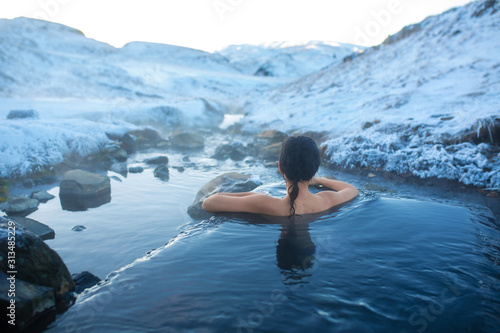 The girl bathes in a hot spring in the open air with a gorgeous view of the snowy mountains. Incredible iceland in winter