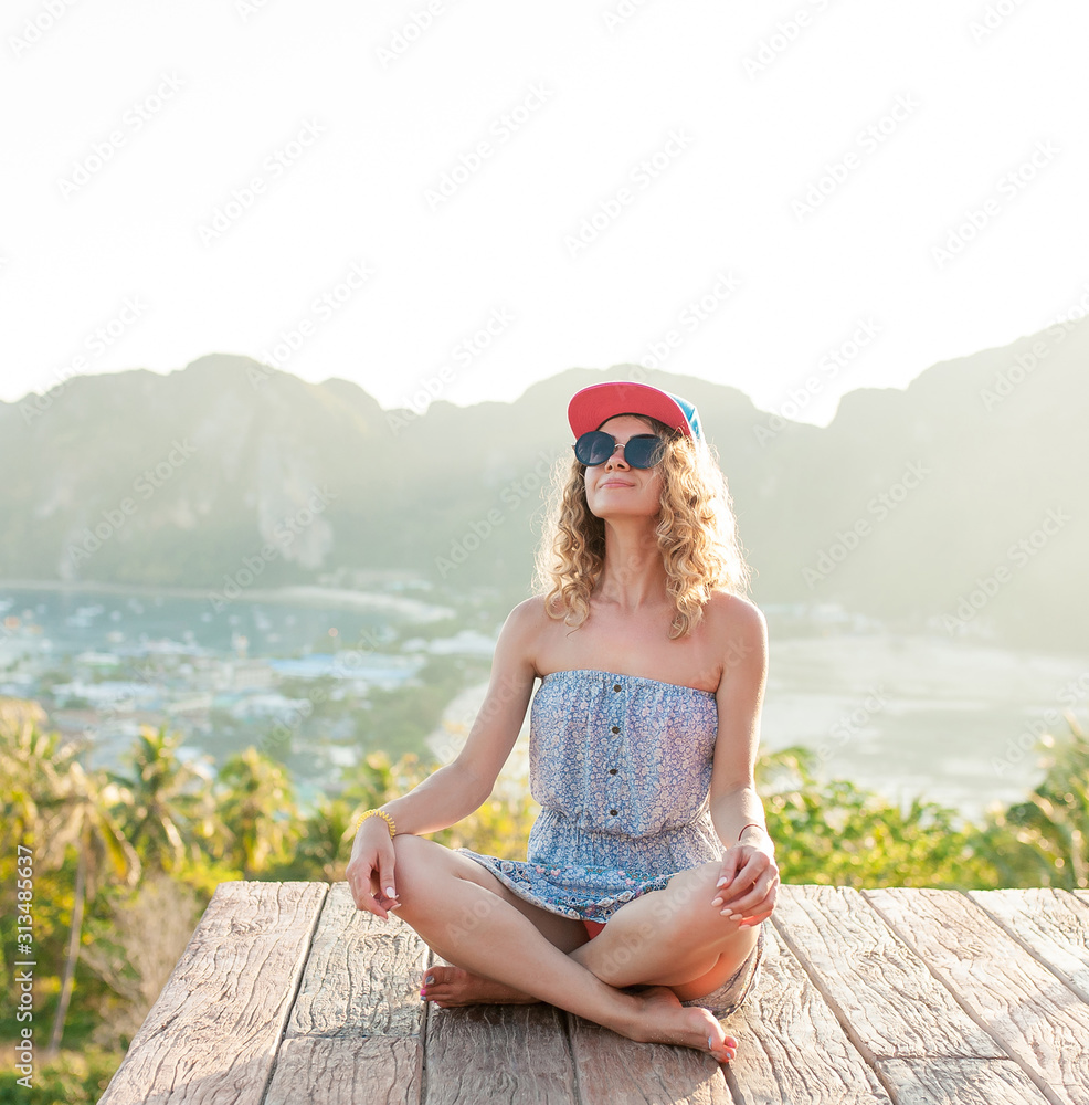 Young woman sitting and enjoying freedom on the top mountains on a sunny day. Portrait of glamour lady enjoying her vacation. Vacation concept. Enjoying the summer. Back view Young woman sitting and enjoying freedom on the top mountains on a sunny day. Portrait of glamour lady enjoying her vacation. Vacation concept. Enjoying the summer. Back view