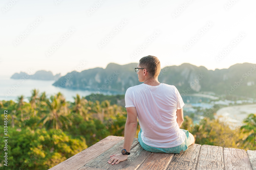 Young man sitting and enjoying freedom on the top view mountains on a sunny day. Portrait of male enjoying him vacation. Vacation concept. Enjoying the summer. Back view
