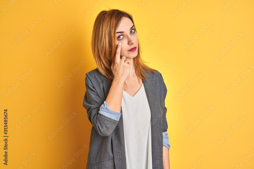 Redhead caucasian business woman over yellow isolated background Pointing with hand finger to the side showing advertisement, serious and calm face Redhead caucasian business woman over yellow isolated background Pointing with hand finger to the side showing advertisement, serious and calm face