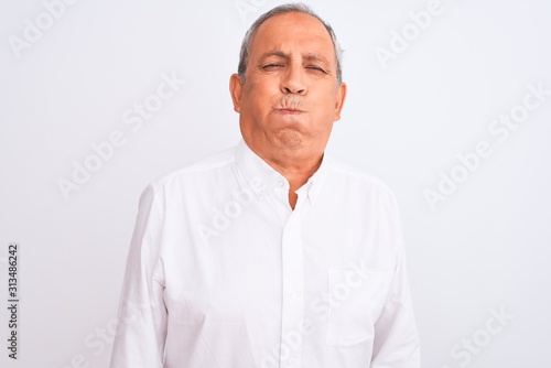 Senior grey-haired man wearing elegant shirt standing over isolated white background puffing cheeks with funny face. Mouth inflated with air, crazy expression. © Krakenimages.com