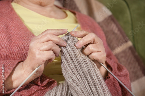 Senior woman knitting warm scarf at home, closeup