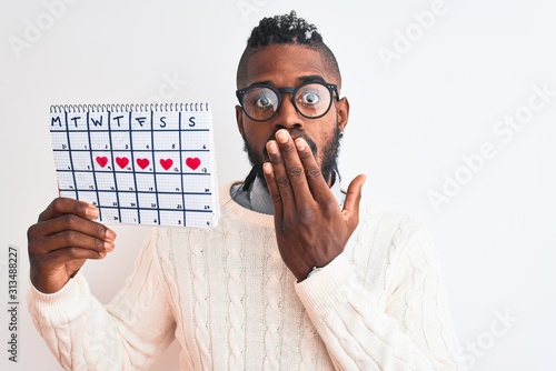 Wallpaper Mural African american man with braids holding period calendar over isolated white background cover mouth with hand shocked with shame for mistake, expression of fear, scared in silence, secret concept Torontodigital.ca