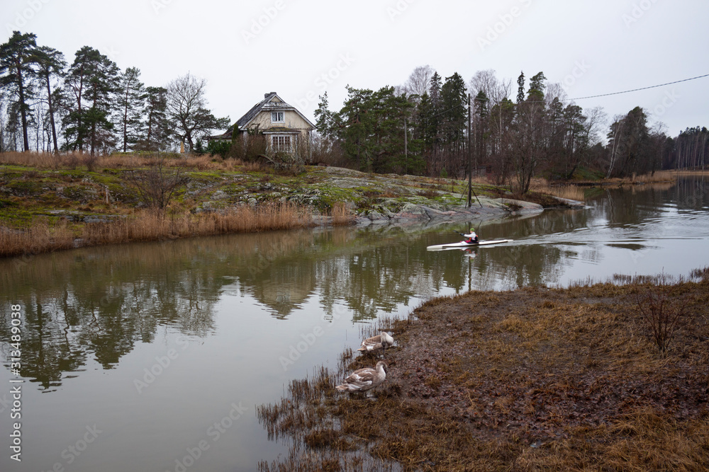 Obraz premium An old authentic rural house and flying trees on the island of Seurasaari is reflected in the lake water on a gloomy autumn day in Helsinki in Finland. Finland autumn landscape