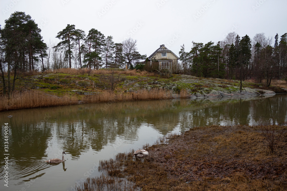 An old authentic rural house and flying trees on the island of Seurasaari is reflected in the lake water on a gloomy autumn day in Helsinki in Finland. Finland autumn landscape An old authentic rural house and flying trees on the island of Seurasaari is reflected in the lake water on a gloomy autumn day in Helsinki in Finland. Finland autumn landscape