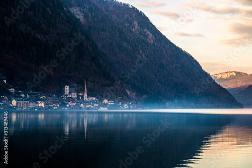 Misty mountains landscape with hills above the lake and old historic village of Hallstatt with buildings reflecting in calm waters of Hallstätter Lake, Dachstein, Austria