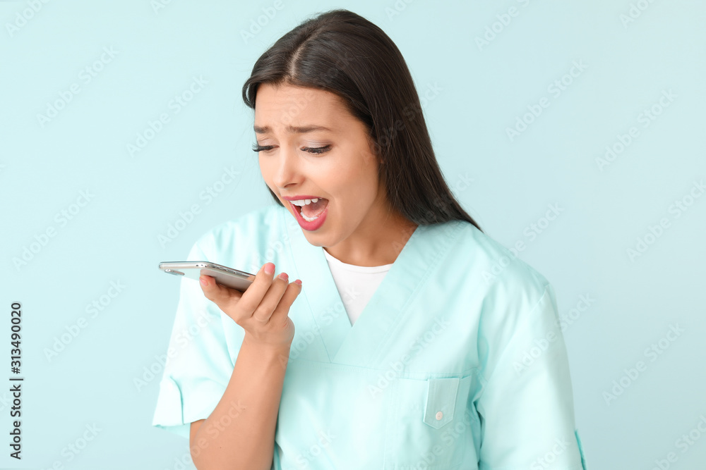 Stressed young nurse talking by mobile phone on color background Stressed young nurse talking by mobile phone on color background