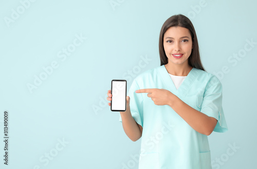 Young nurse with mobile phone on color background