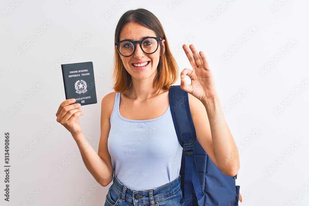 Beautiful redhead student woman wearing backpack and holding passport of italy doing ok sign with fingers, excellent symbol