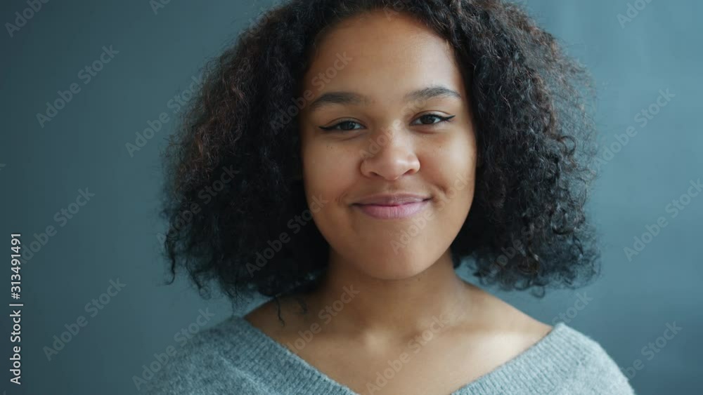 Portrait of young cheerful African American woman smiling standing alone on dark gray background looking at camera. Positive emotions and people concept. Portrait of young cheerful African American woman smiling standing alone on dark gray background looking at camera. Positive emotions and people concept.