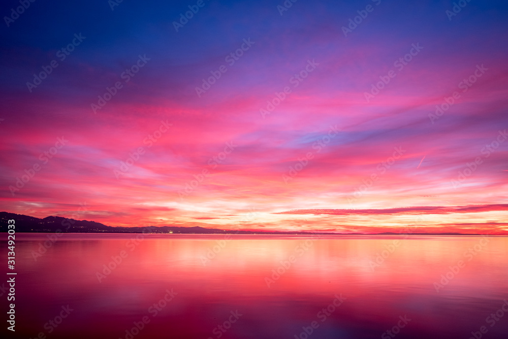 dark violet clouds with orange sun light and pink light in wonderful twilight sky on lake Bodensee in Lindau