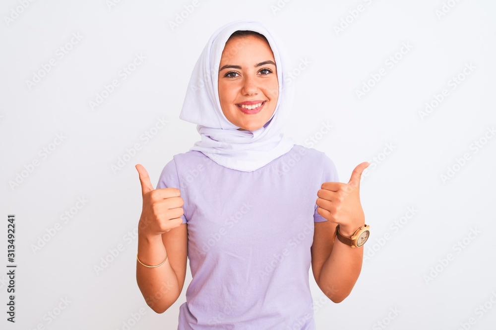 Young beautiful arabian girl wearing hijab standing over isolated white background success sign doing positive gesture with hand, thumbs up smiling and happy. Cheerful expression and winner gesture. Young beautiful arabian girl wearing hijab standing over isolated white background success sign doing positive gesture with hand, thumbs up smiling and happy. Cheerful expression and winner gesture.