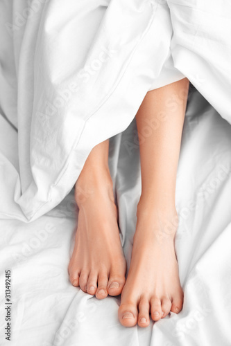 Morning at Home. Woman lying on bed legs under blanket top view close-up