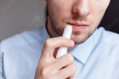 Man applying hygienic lipstick on lips to revive chapped lips and avoid dry, closeup photo